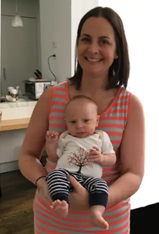 A mother smiling while holding a baby in her arms at home